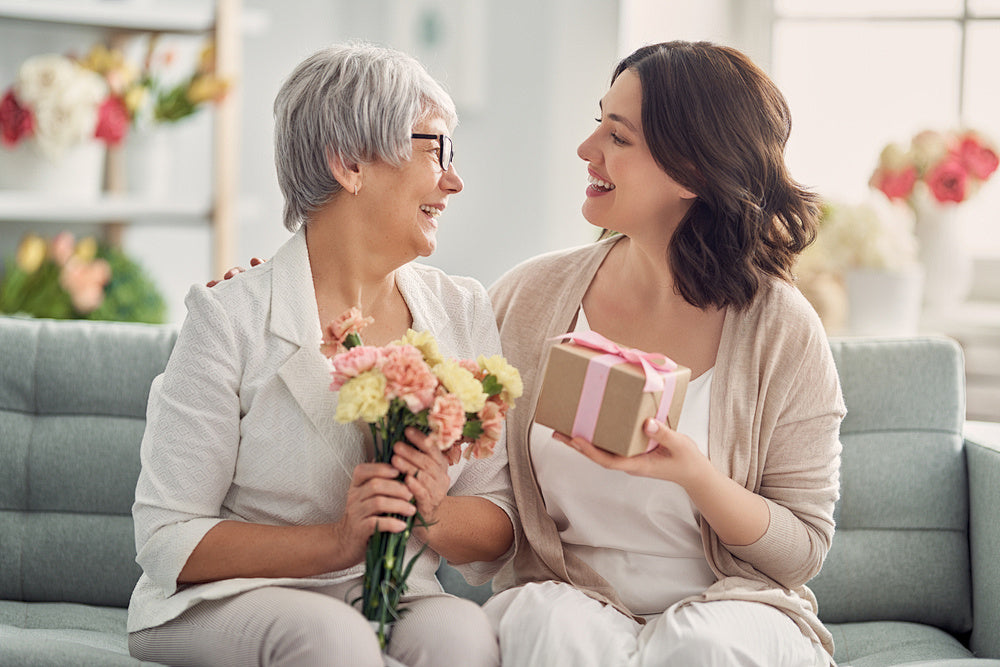 Two women sharing a joyful moment with a Mother's Day gift and flowers in a cozy living room