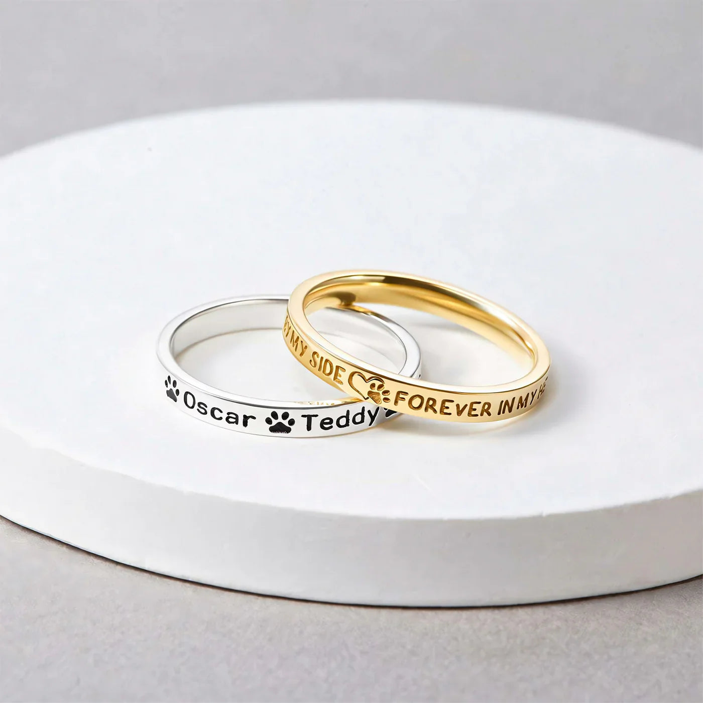 Custom Pet Name Ring set showing silver and gold engraved bands with paw prints and names Oscar and Teddy on white tray